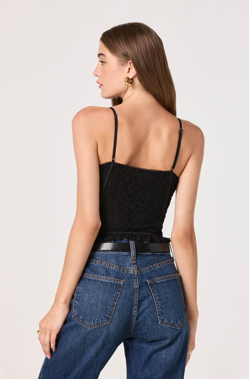 A woman is wearing a black lace spaghetti strap top paired with high-waisted blue jeans and a black belt. She accessorized with gold earrings and a ring on her finger.
