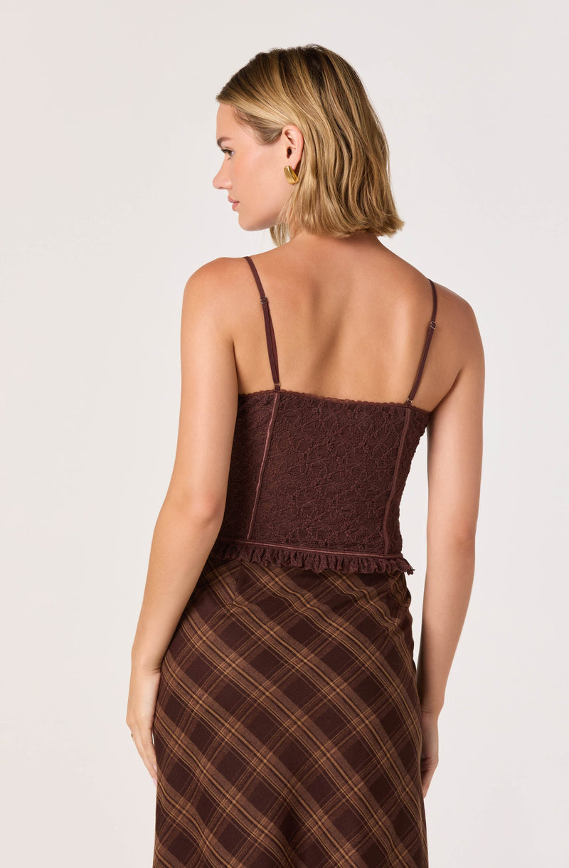A woman is wearing a fitted, spaghetti strap, maroon lace top with a ruffled hem. She is also wearing a high-waisted, brown plaid skirt with diagonal lines. The outfit has warm earthy tones.