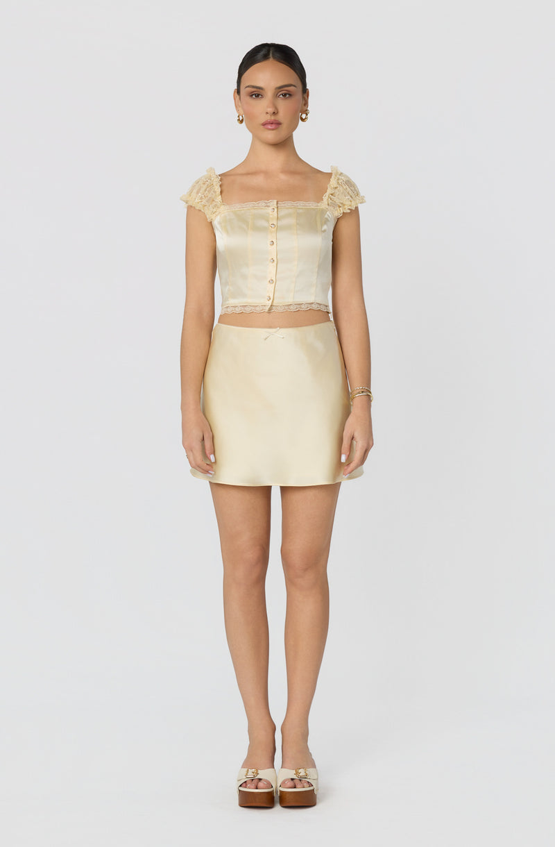 Woman in a cream satin two-piece outfit with ruffled cap sleeves and a mini skirt.
