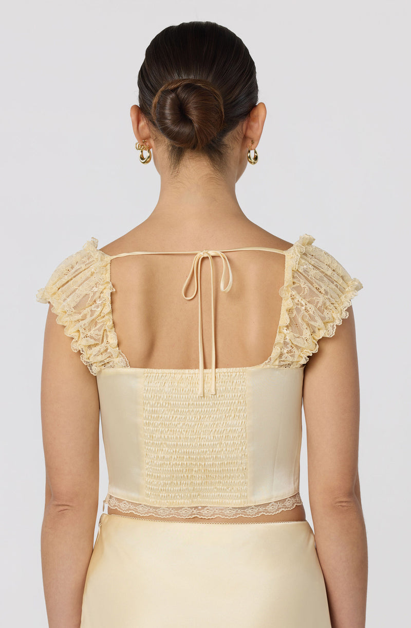 Back view of a woman wearing a cream-colored outfit with ruffled lace shoulder straps and a laced corset top.
