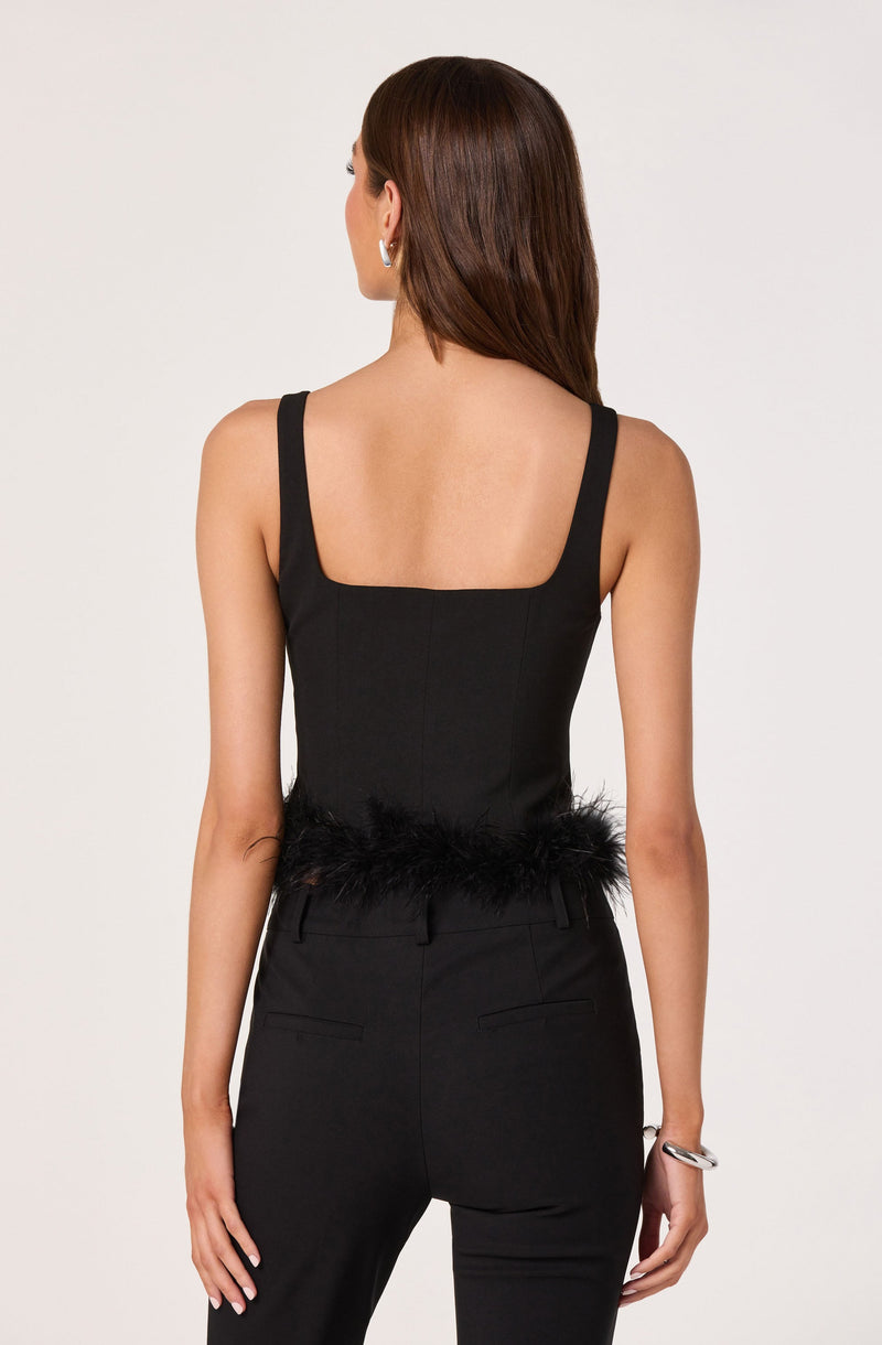 A woman is wearing a sleeveless black top with wide shoulder straps and a square neckline, paired with high-waisted black trousers. The top features a feathered trim at the waistline.