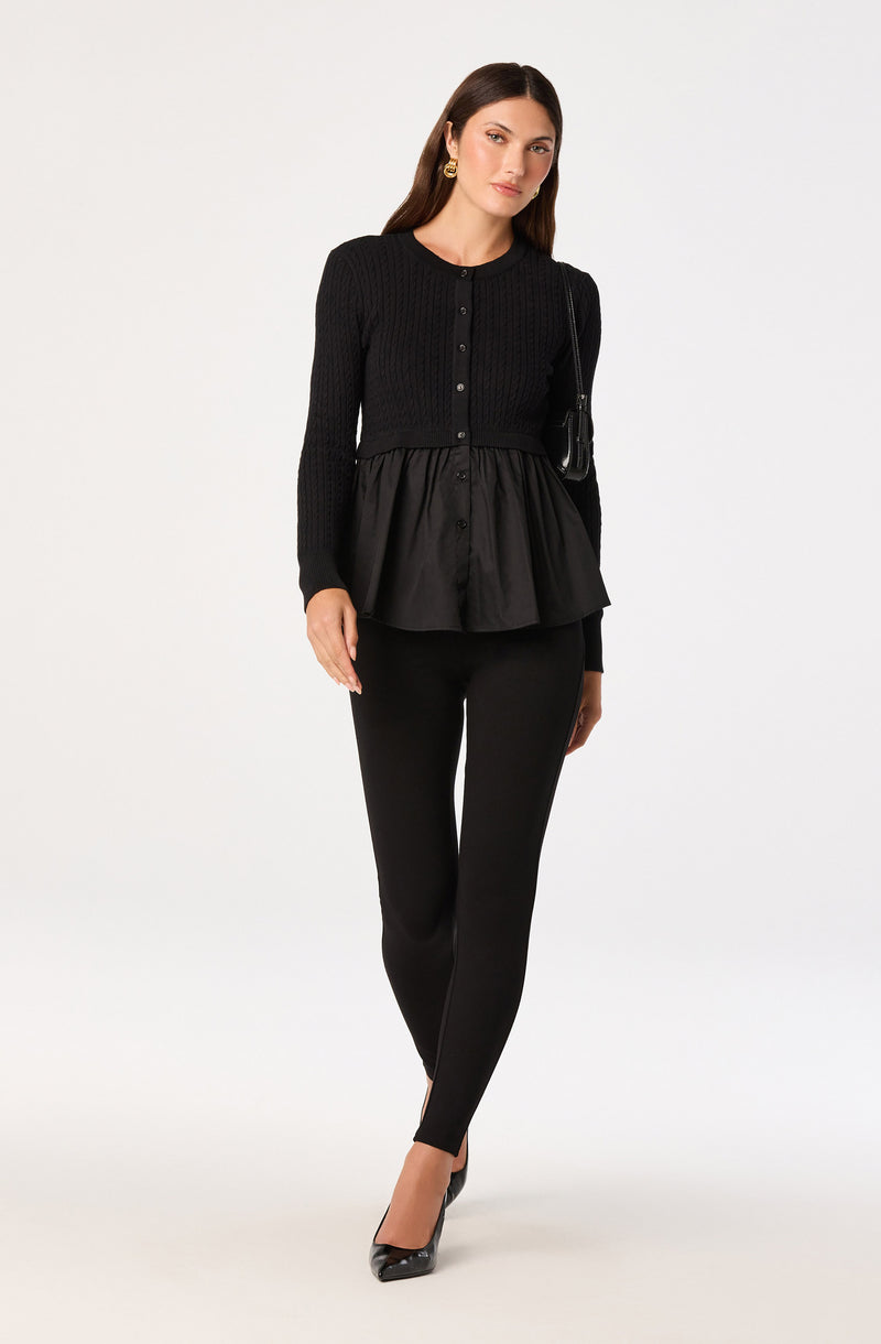 Woman wearing a black long-sleeve knit top with a peplum hem, black fitted pants, and black heels.