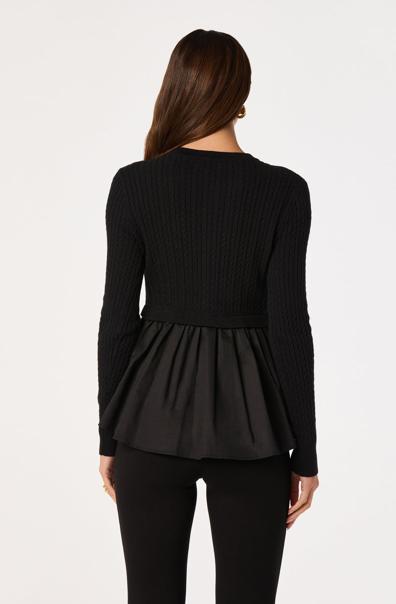 Woman wearing a black long-sleeve knit sweater with a pleated satin peplum.
