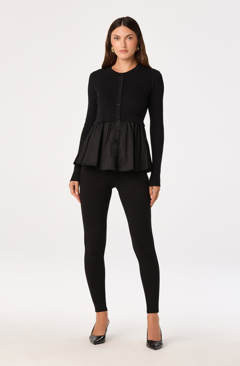 Woman wearing a long-sleeve black knit top with a peplum hem and black skinny pants.