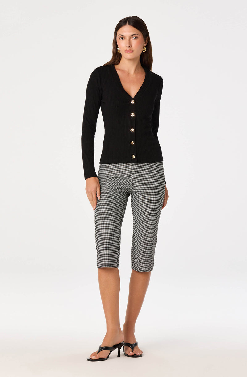Woman wearing a black button-up cardigan with floral details and gray checkered cropped pants.