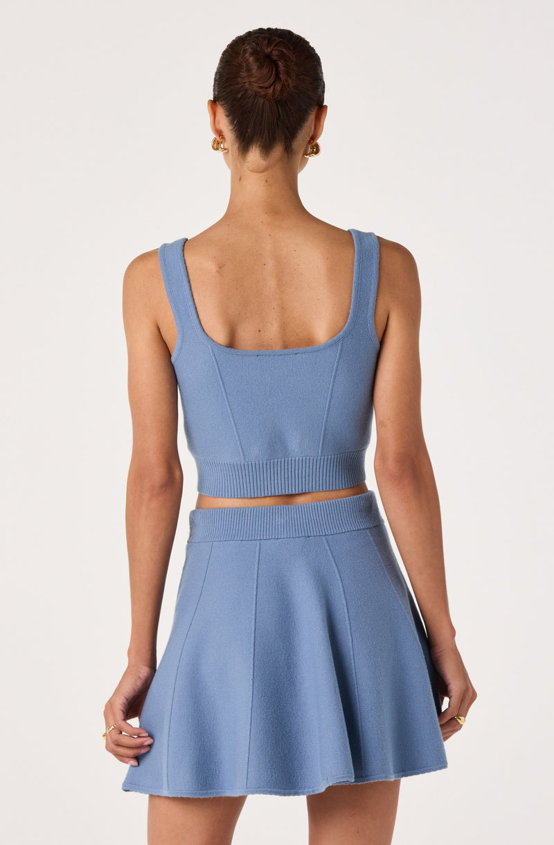 Blue sleeveless crop top with wide straps and matching high-waisted skirt with pleats.