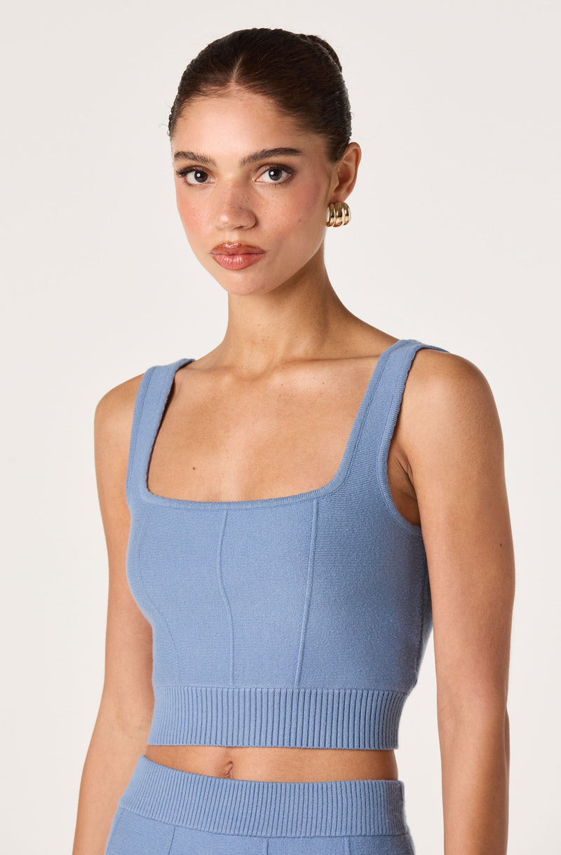 Woman wearing a light blue sleeveless cropped top with wide straps and a ribbed hem.