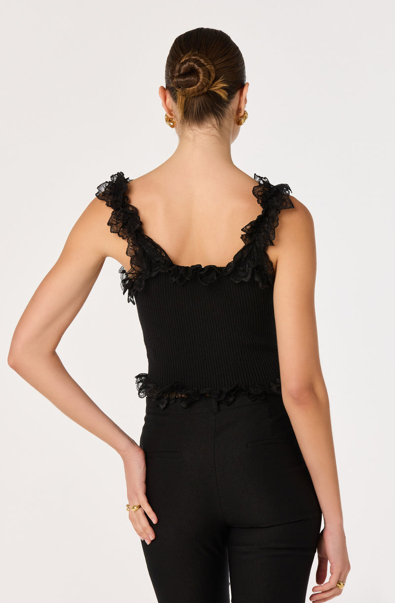 Woman in black sleeveless top with ruffled lace shoulder details and high-waisted black pants.