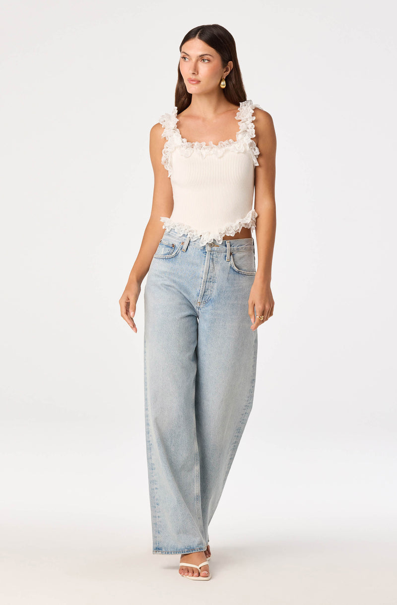 Woman in a white sleeveless top with ruffle details and light-wash wide-leg jeans.