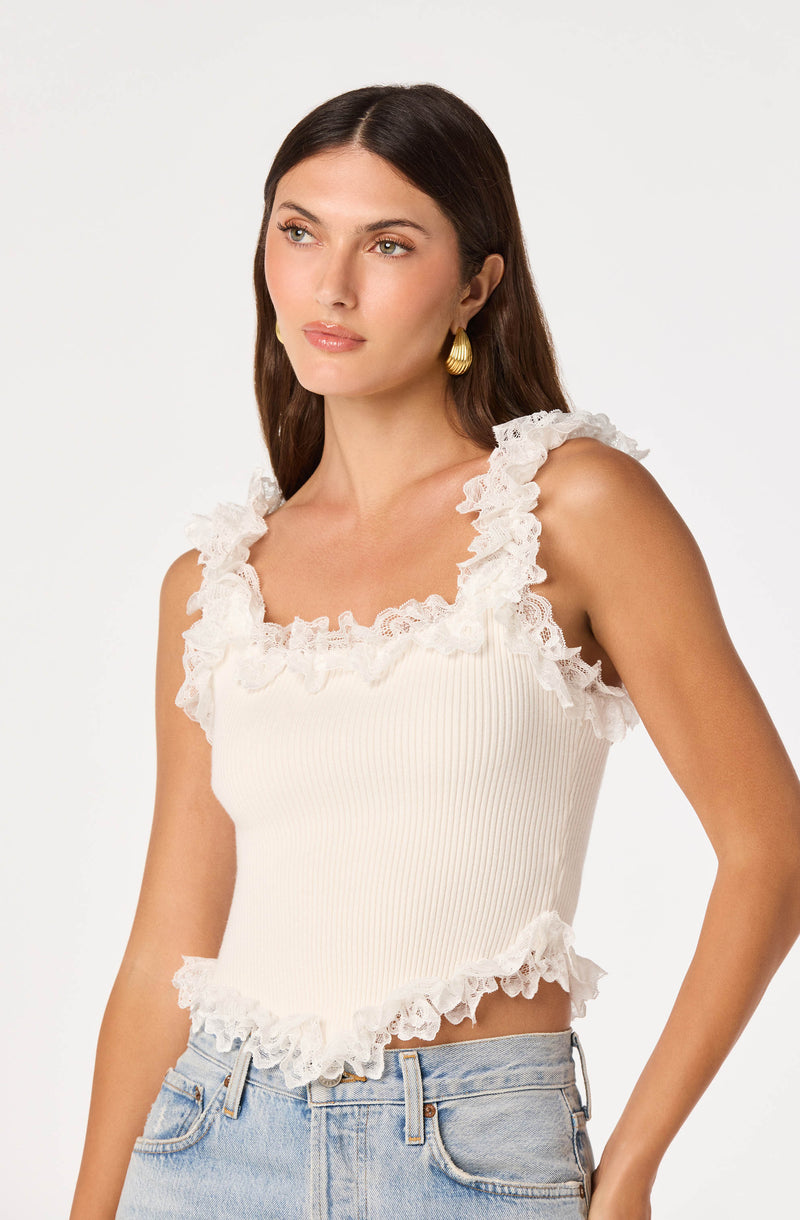 Woman in white sleeveless top with ruffled lace trim and light blue jeans.
