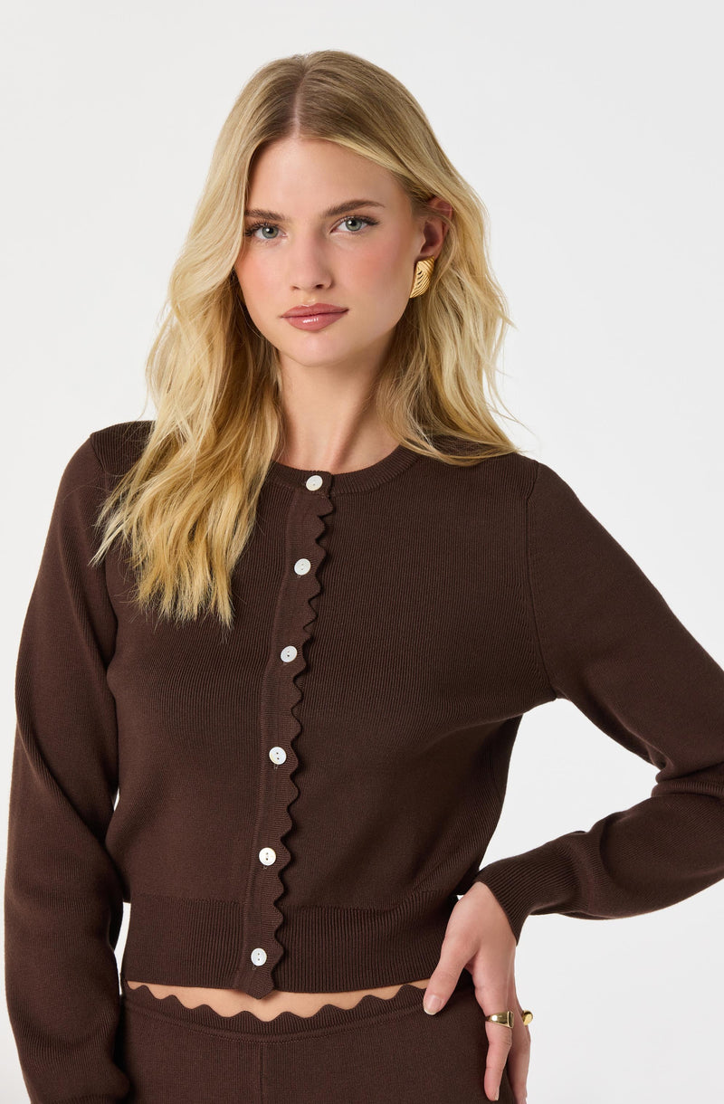 Woman wearing a brown button-up sweater with a wavy trim detail, and matching brown pants.