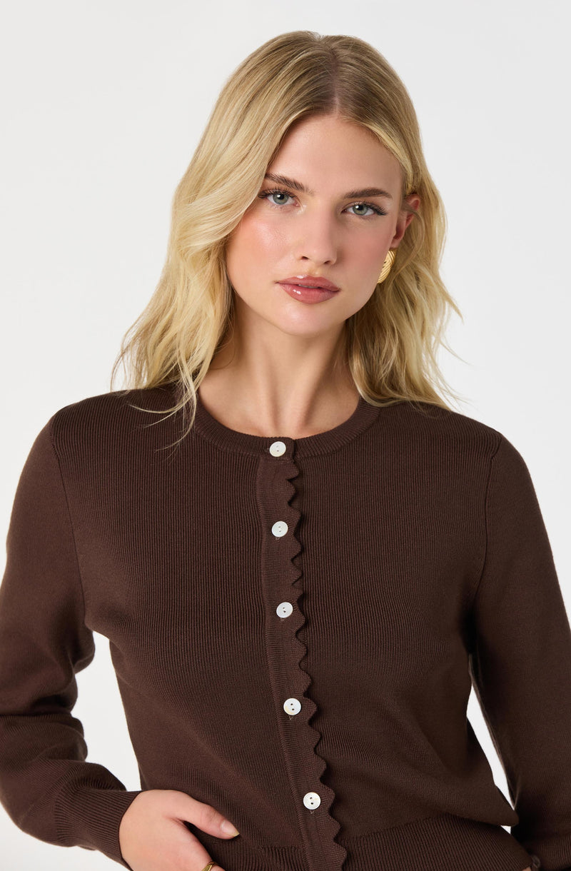 Woman wearing a brown cardigan with white buttons, ruffled detail down the front.