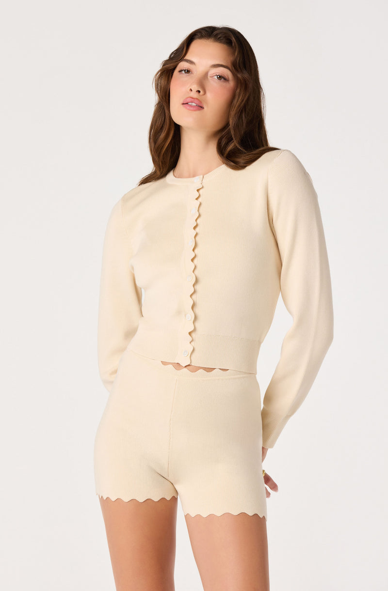 Woman in cream matching sweater and shorts, both with scalloped edges.