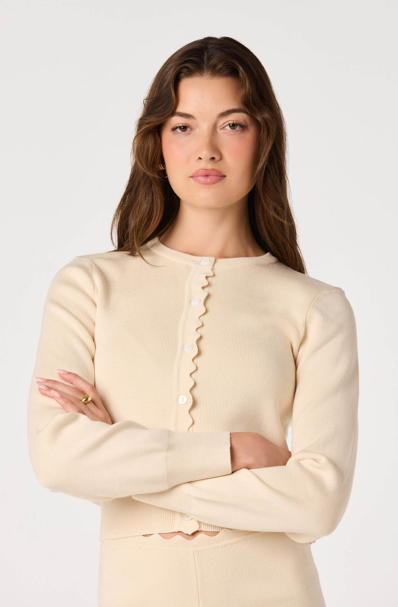 Cream-colored cardigan with ruffled button placket and matching skirt or pants.