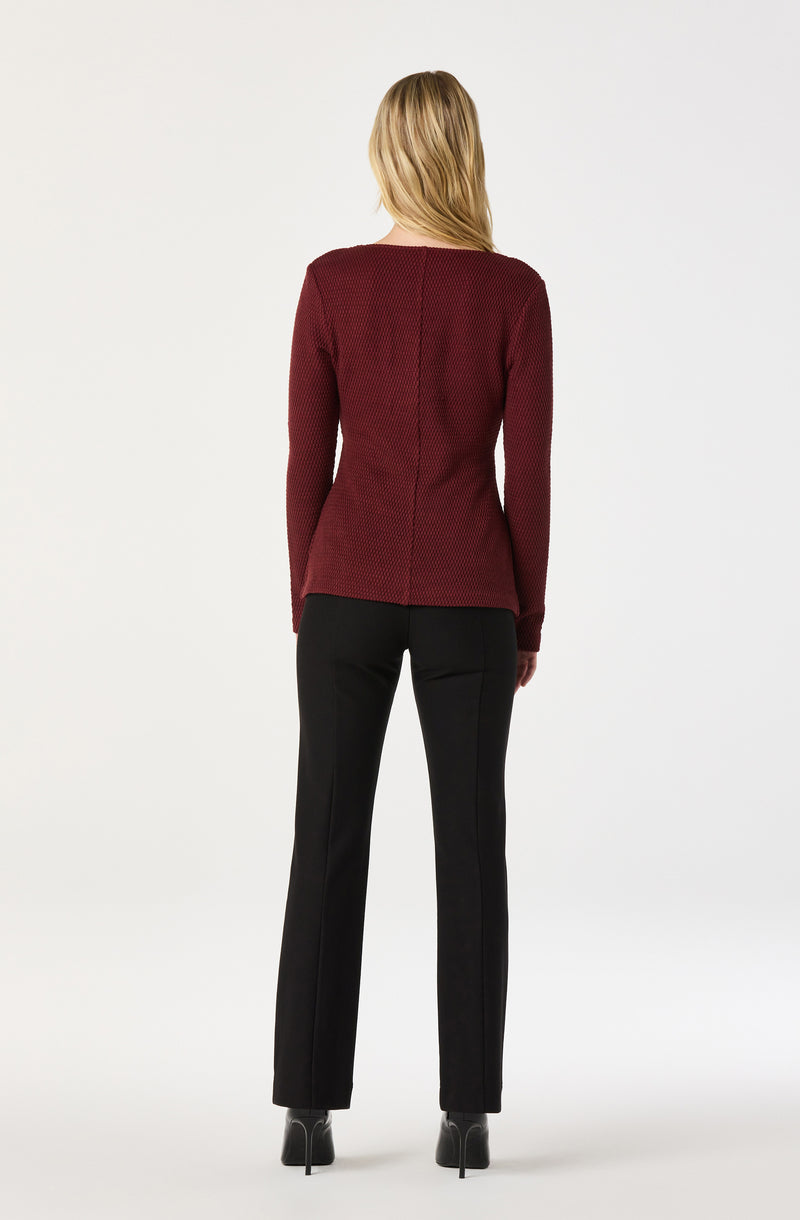 A woman seen from the back is wearing a long-sleeved, textured deep red sweater and black fitted pants with a straight-leg cut. She is also wearing black heeled shoes.