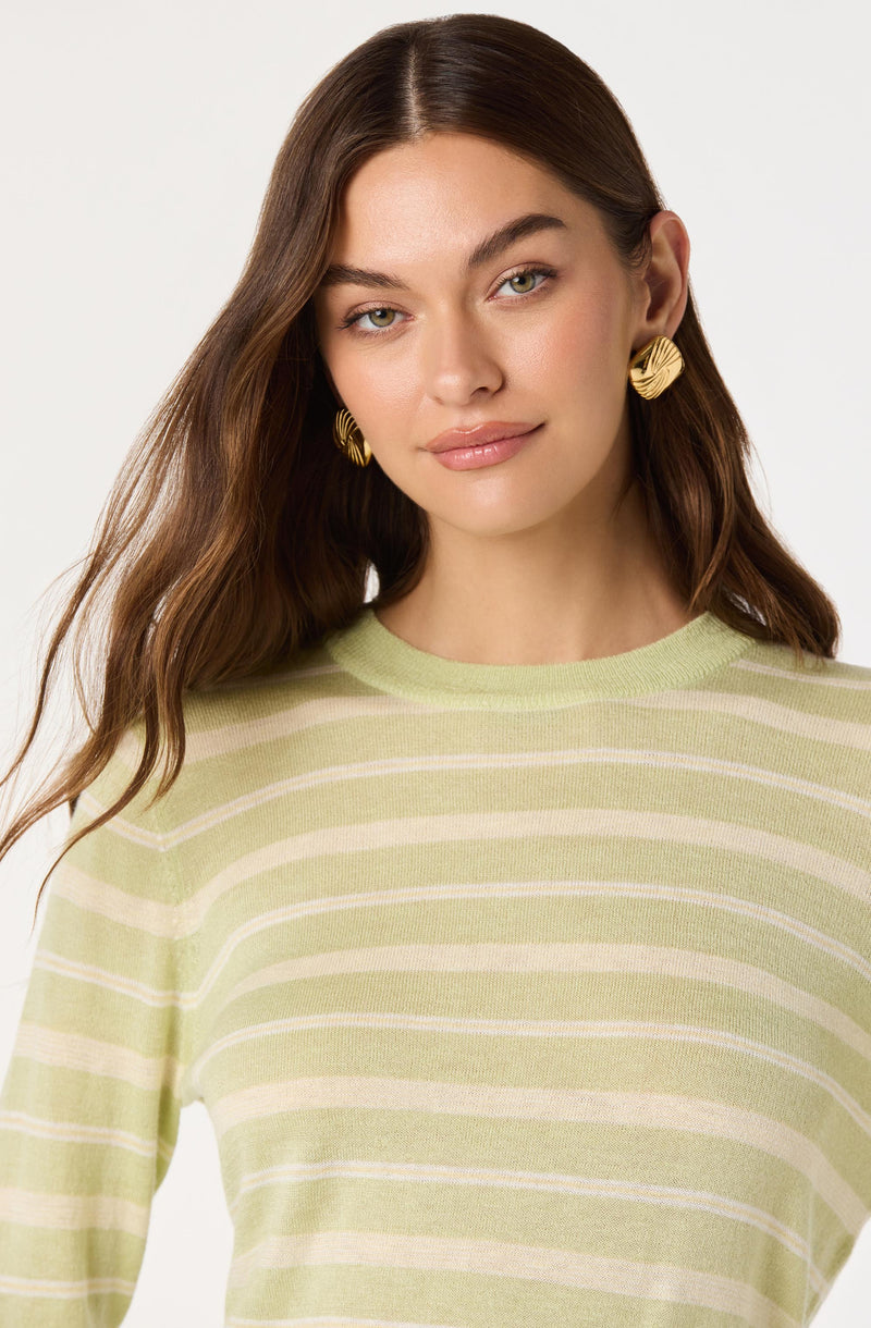 A woman is wearing a light green and cream horizontal striped sweater with a round neckline. She has gold, textured, spiral-shaped earrings.