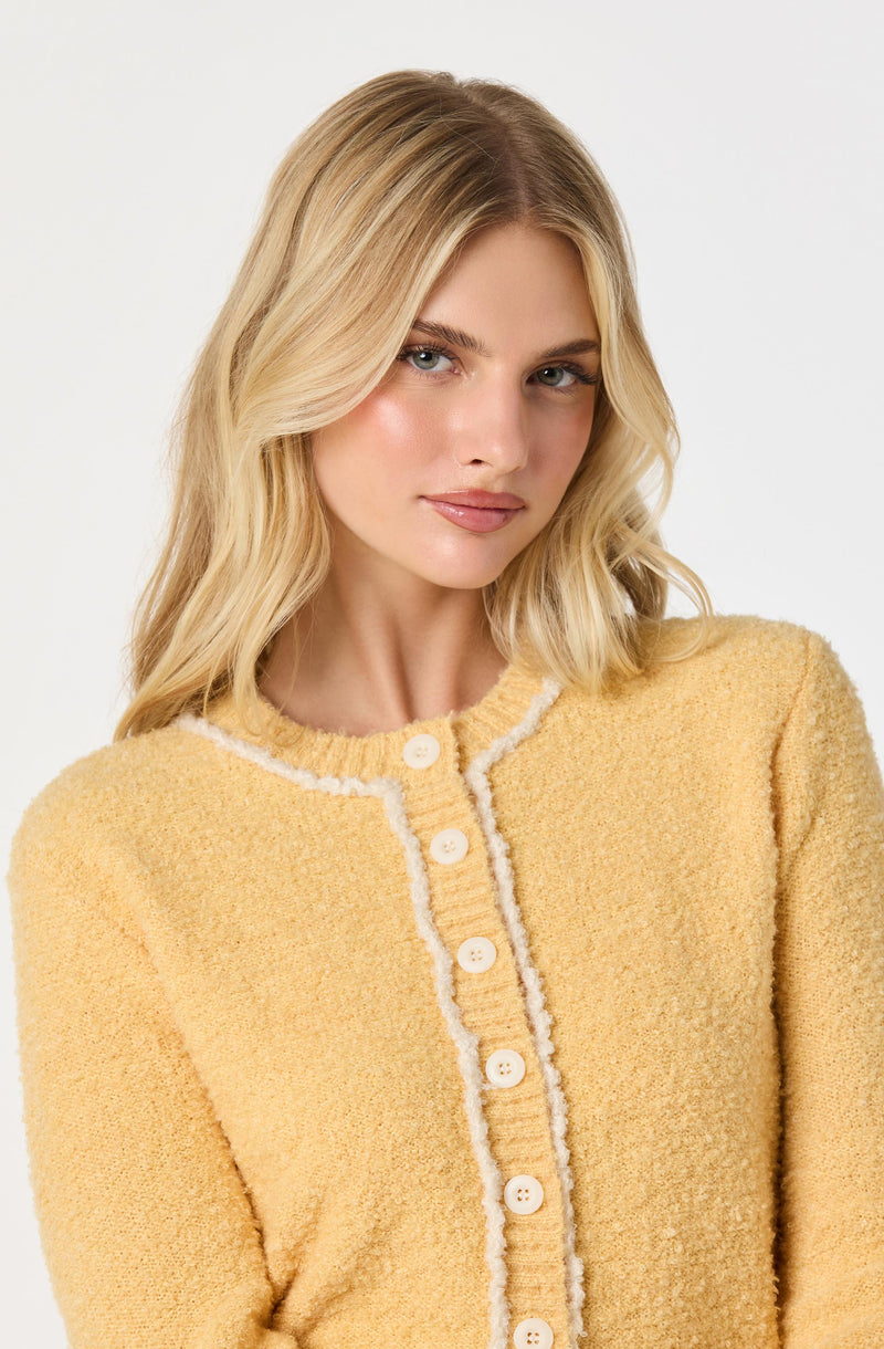 A woman wearing a soft, textured, yellow cardigan with white trim along the edges and white buttons down the front.