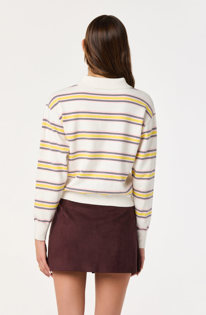 A woman is wearing a long-sleeved, collared sweater with horizontal stripes in yellow, navy, and pink on a white background. She is also wearing a maroon suede mini skirt.