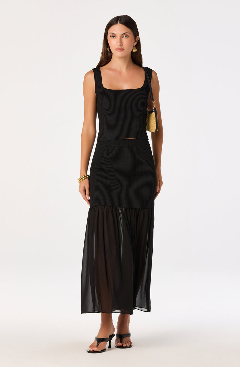 Woman wearing a sleeveless black ribbed top and a black sheer skirt.