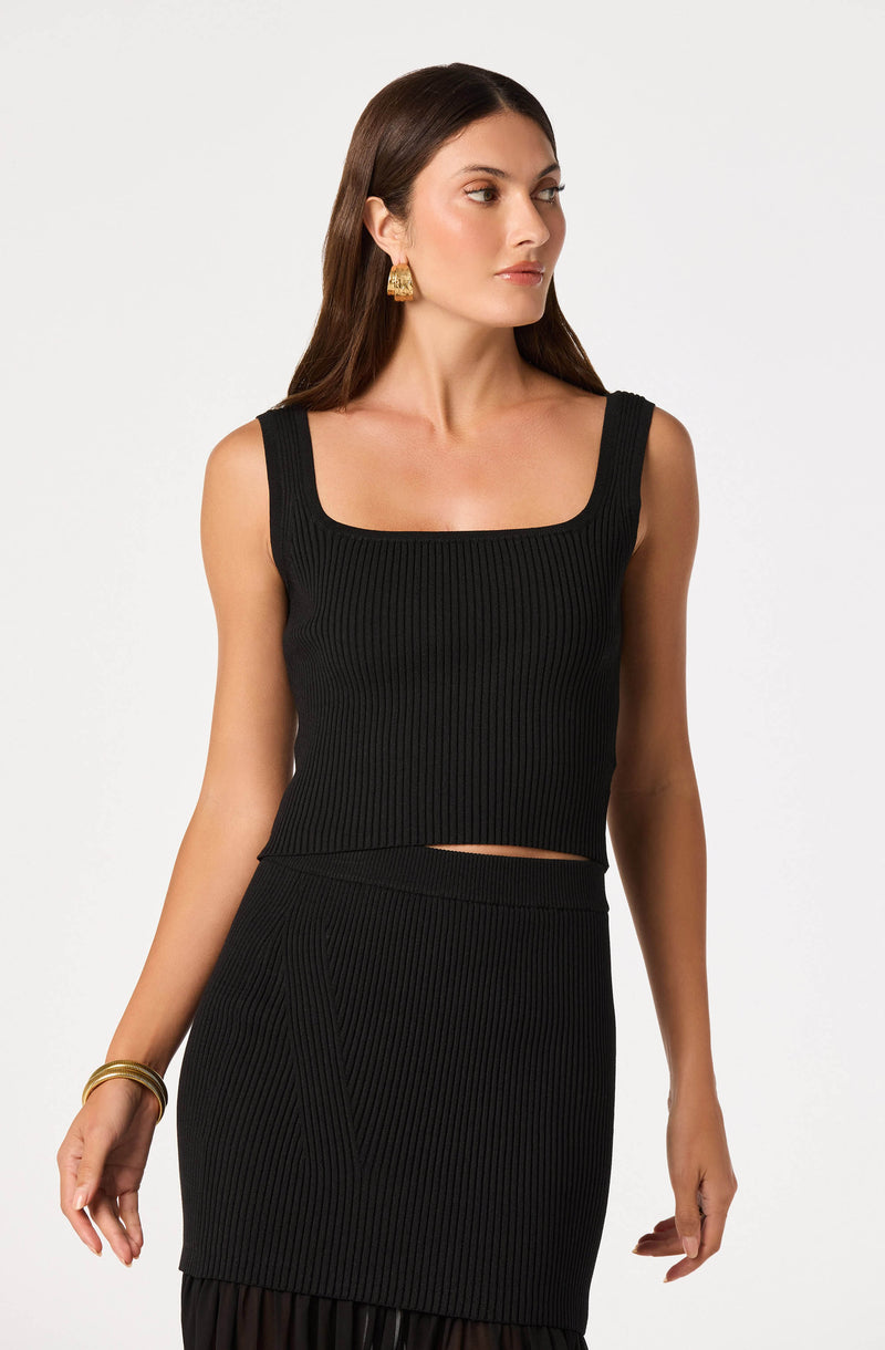 Woman wearing a black, ribbed, sleeveless crop top and matching high-waisted skirt.