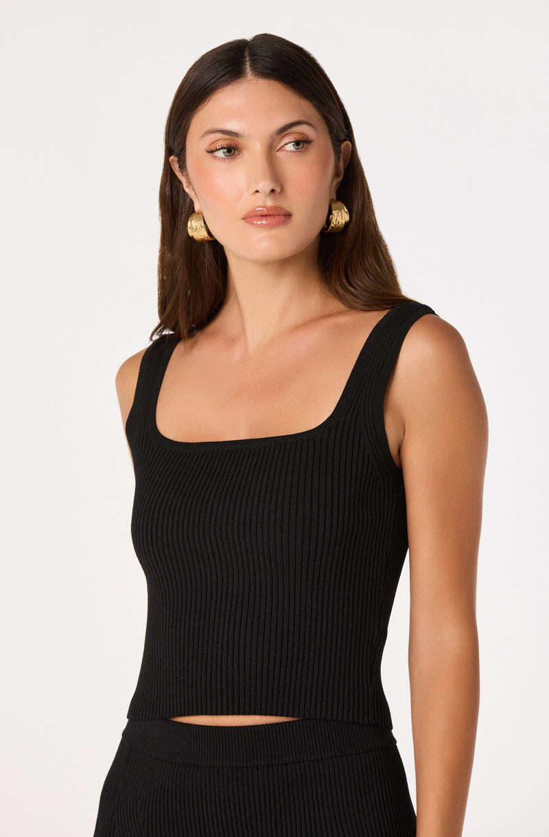 Woman wearing a sleeveless black ribbed tank top with wide straps.