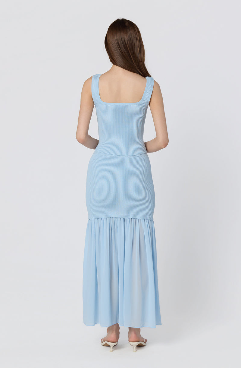 Woman in a light blue sleeveless ribbed dress with a gathered skirt at the bottom.
