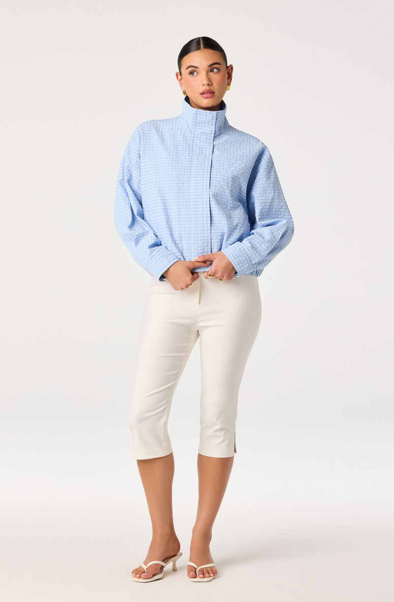 Woman in light blue checkered blouse with a high collar, white cropped pants, and nude heels.