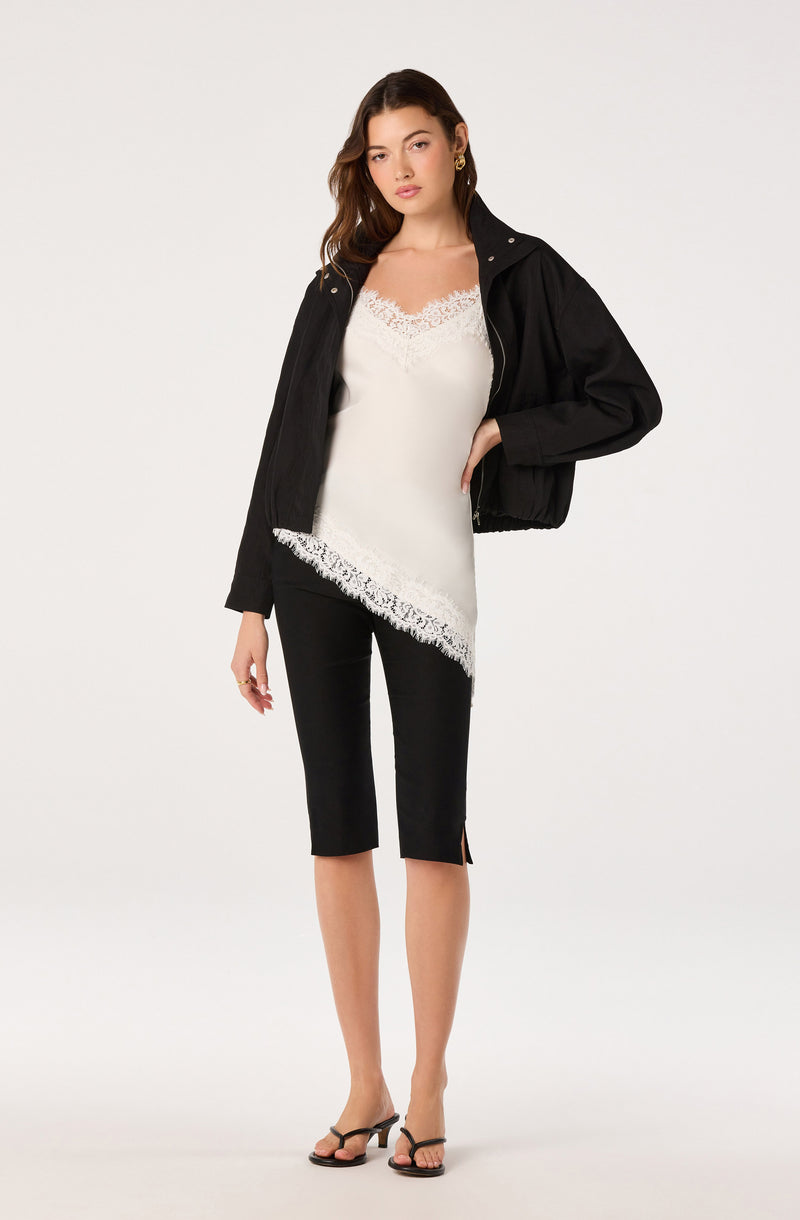 Woman wearing a black jacket, white top with lace, black cropped pants, and black heels.