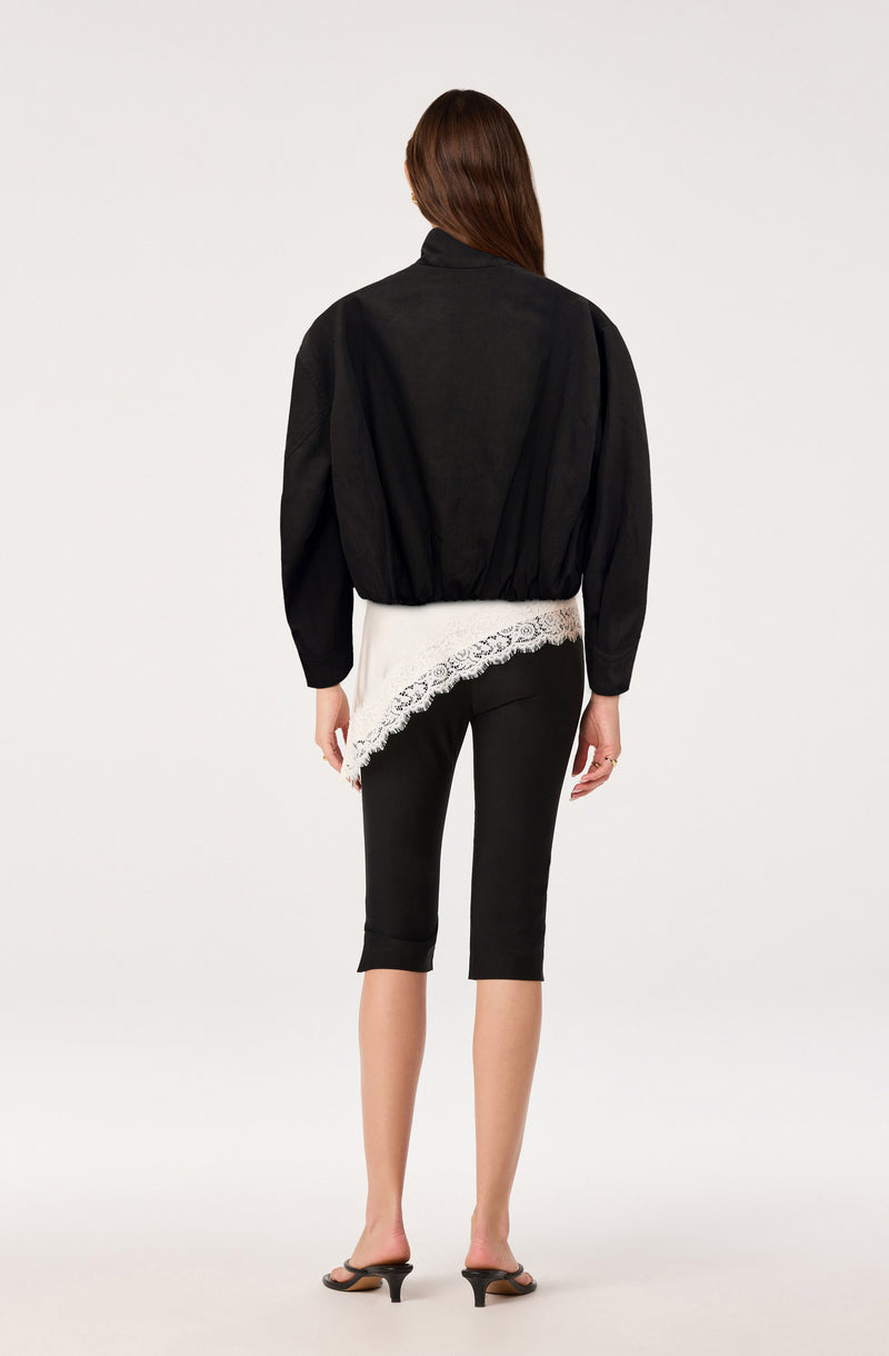 Woman in black jacket, black capri pants, and black heeled sandals, with a white lace detail peeking out from underneath the jacket.