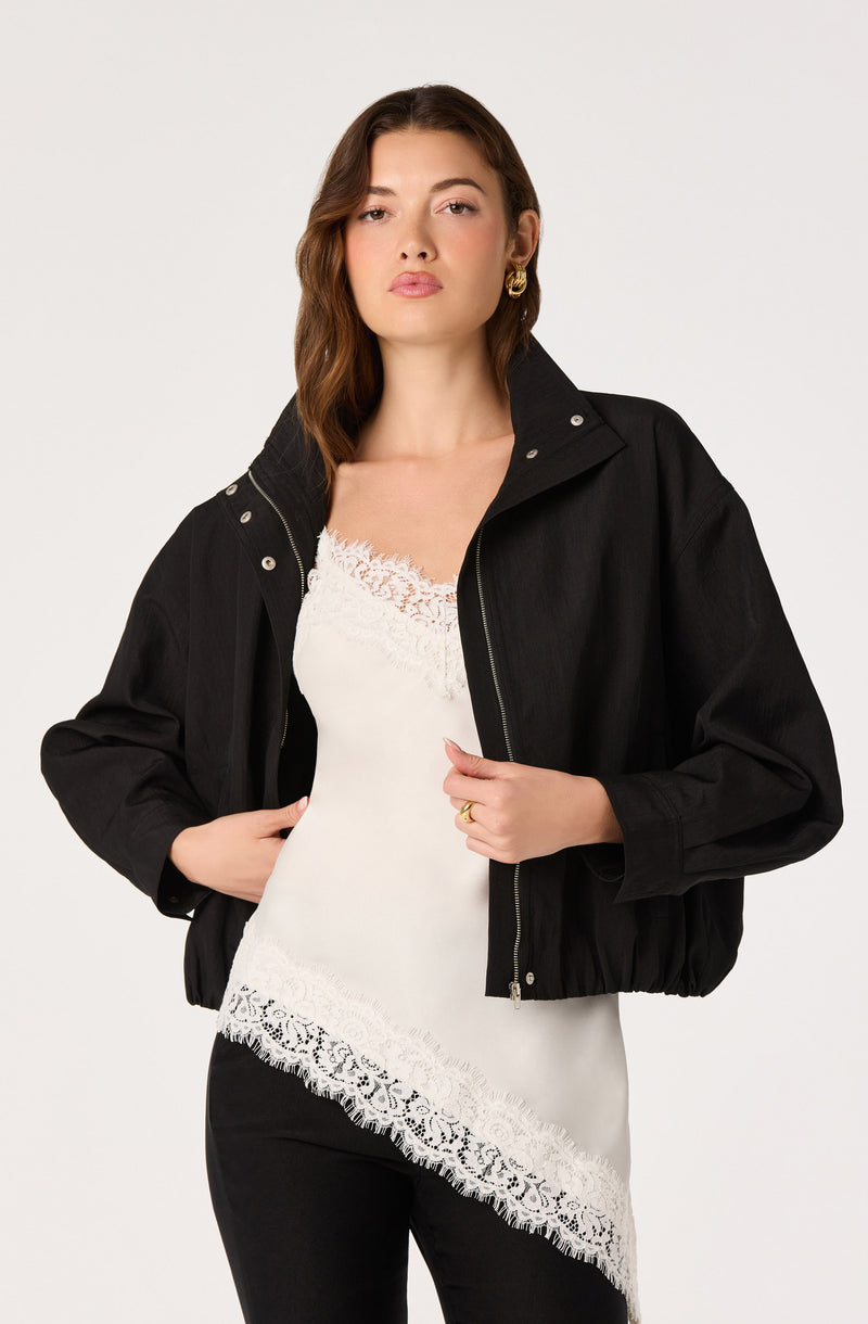 Woman wearing a black jacket over a white lace-trimmed top.