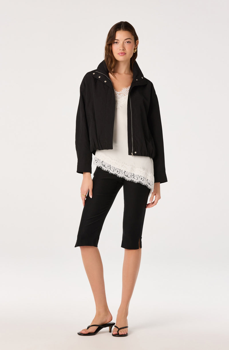 Woman wearing a black cropped jacket, white lace top, black knee-length pants, and black sandals.