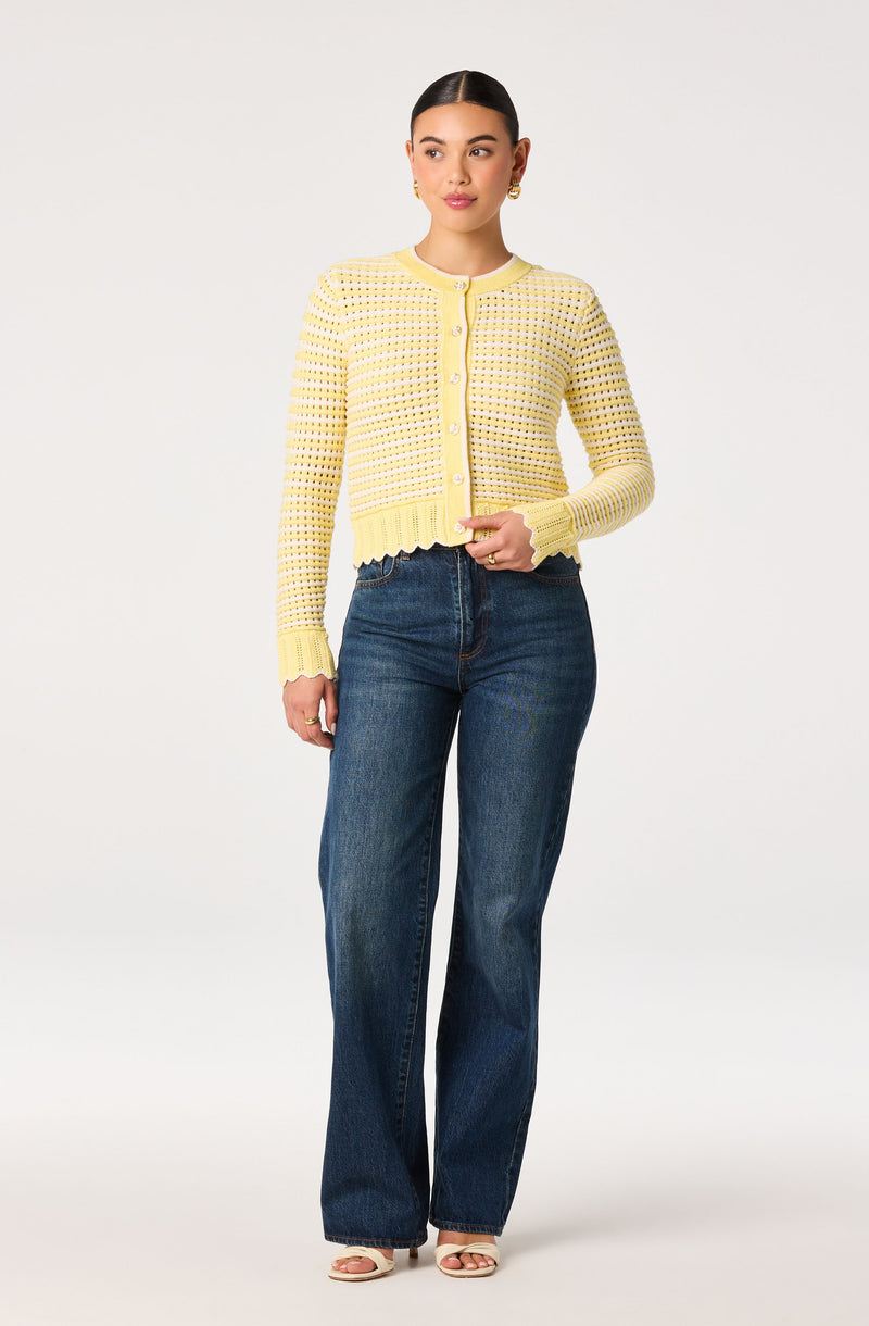 Woman wearing a yellow knit cardigan with pearl buttons and dark blue jeans.