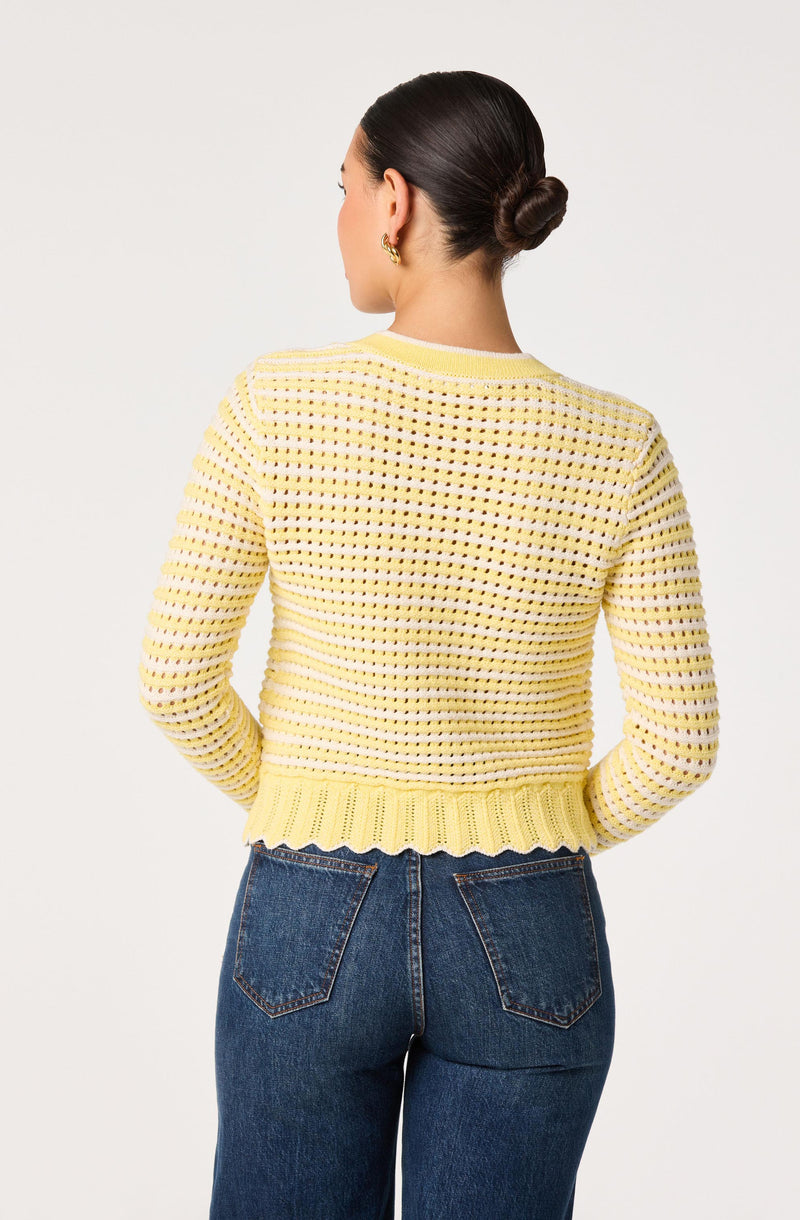 Woman wearing a yellow knitted sweater with a scalloped hem.