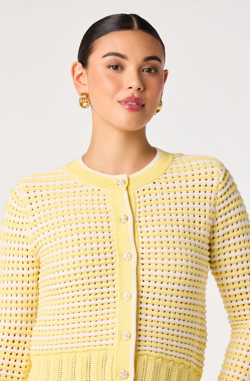 Woman wearing a yellow, textured, button-up cardigan with pearl-embellished buttons and gold hoop earrings.