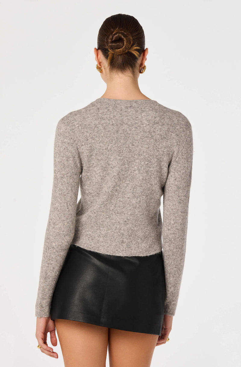 Woman wearing a gray knit sweater and a black leather mini skirt, with her hair in a bun.