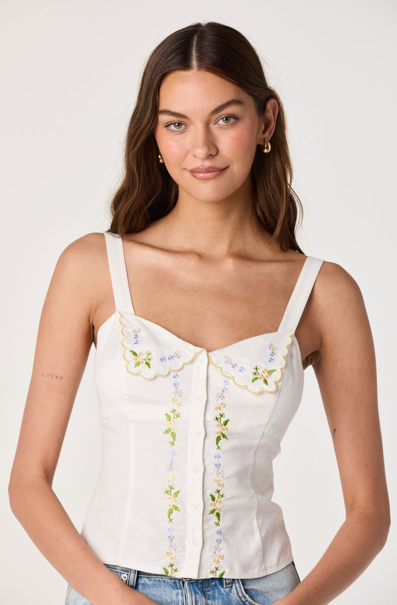 White sleeveless top with embroidered floral details and a scalloped collar.