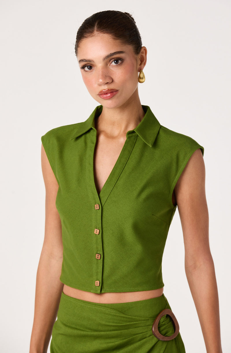 Woman in a sleeveless, green, collared crop top with buttons and a matching green skirt with a large ring detail.