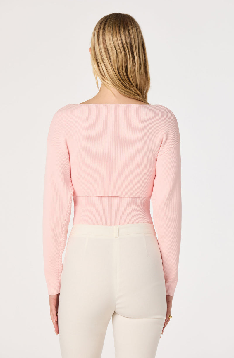 Woman wearing a light pink ribbed cropped sweater and high-waisted white pants.