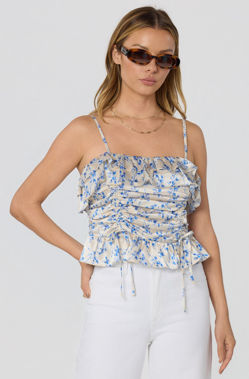Beige floral ruffled sleeveless top with thin straps, paired with white pants.