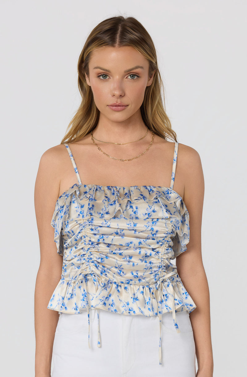 Woman in a beige and blue floral ruffled sleeveless top with thin straps.