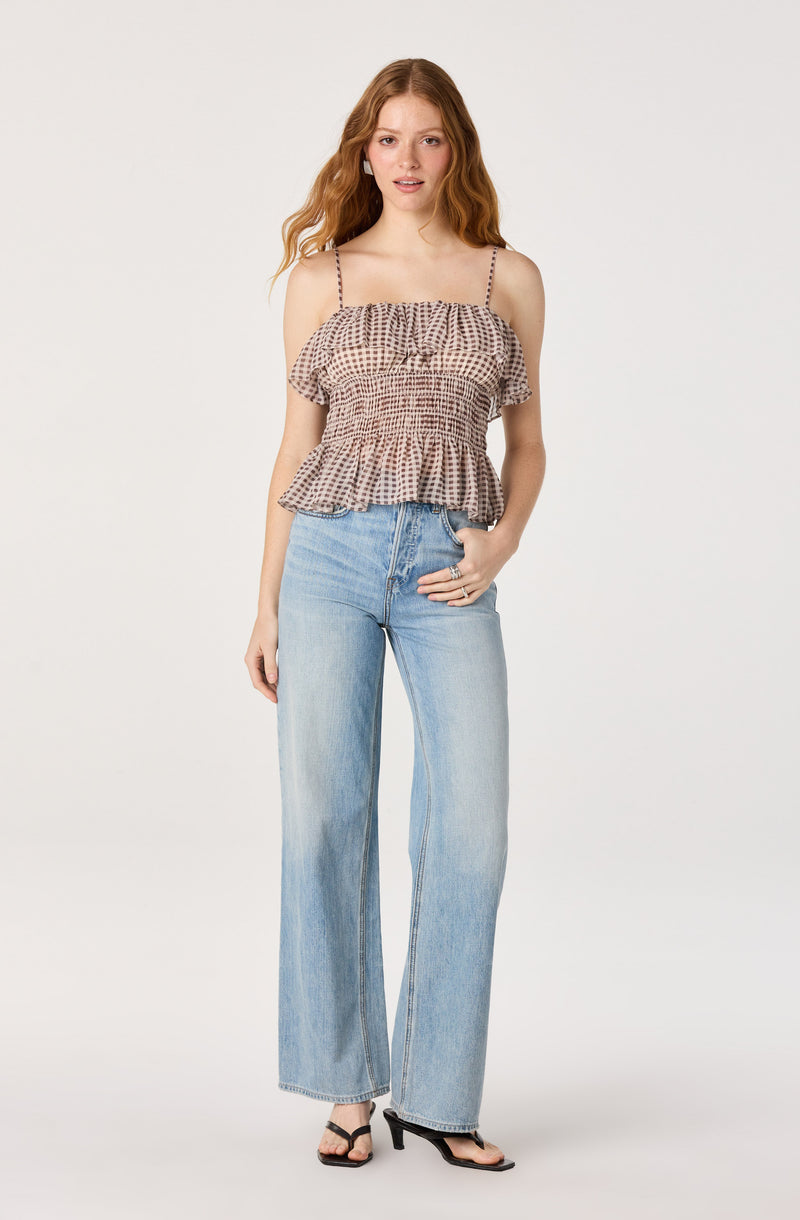 Woman in a beige checkered ruffled top with spaghetti straps and light blue high-waisted jeans.