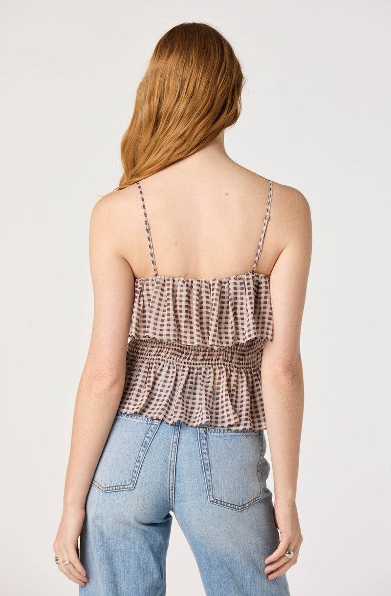 Back view of a woman wearing a brown checkered sleeveless top with thin straps and elastic waistband, paired with light blue jeans.