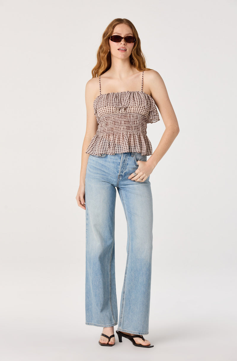 Woman wearing a checkered spaghetti strap top with ruffled hem, light blue wide-leg jeans, black heeled sandals, and sunglasses.
