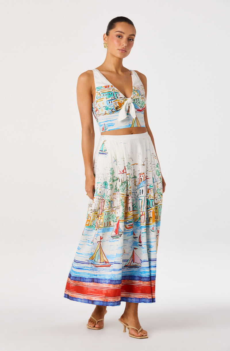 Woman wearing a colorful, nautical print crop top and wide-leg pants with sailboats and coastal scene patterns.