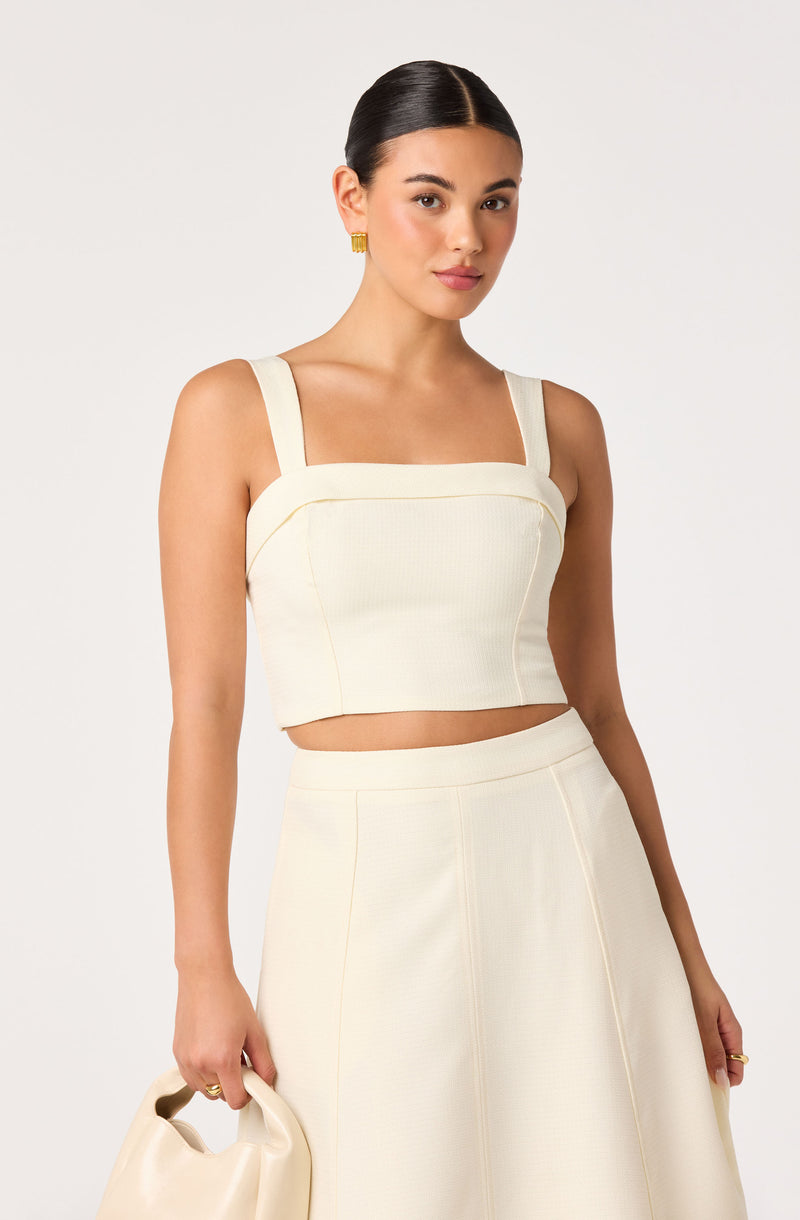 Woman in white two-piece outfit with a sleeveless crop top and high-waisted skirt.