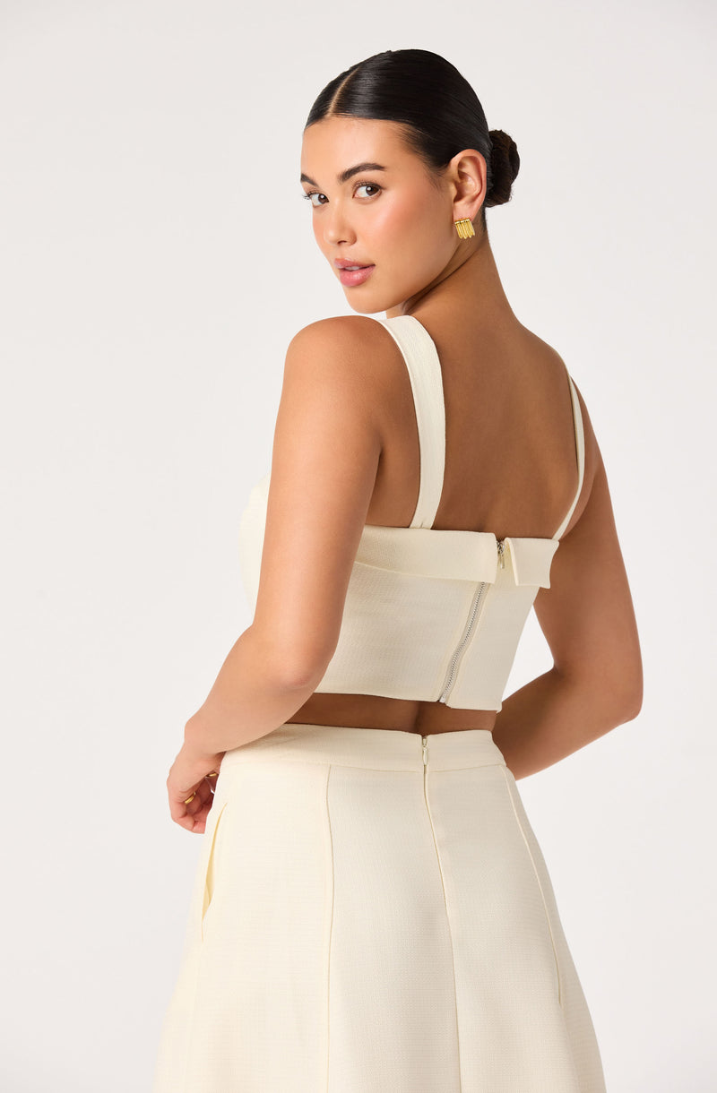 Woman wearing a cream-colored crop top with wide straps and matching high-waisted skirt.