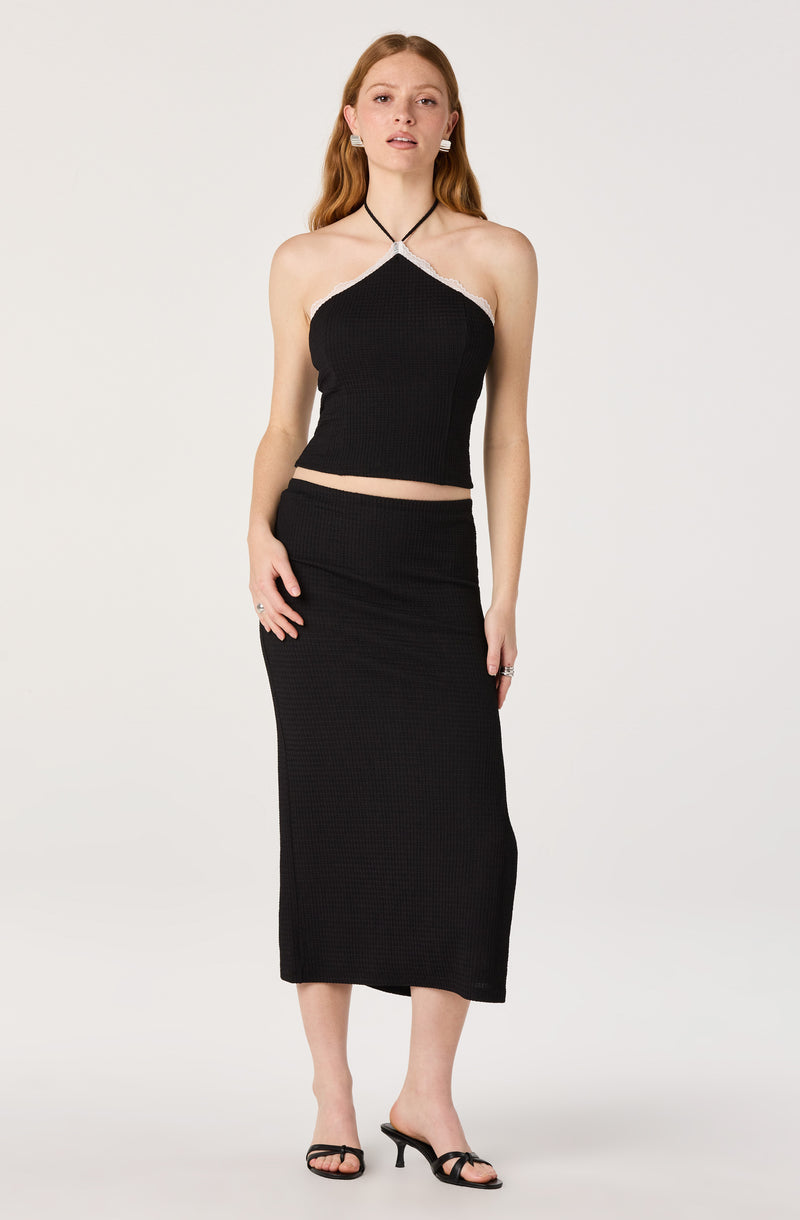 Woman wearing a black halter top with white trim and a matching black long skirt with a slight slit, paired with black high-heeled sandals.