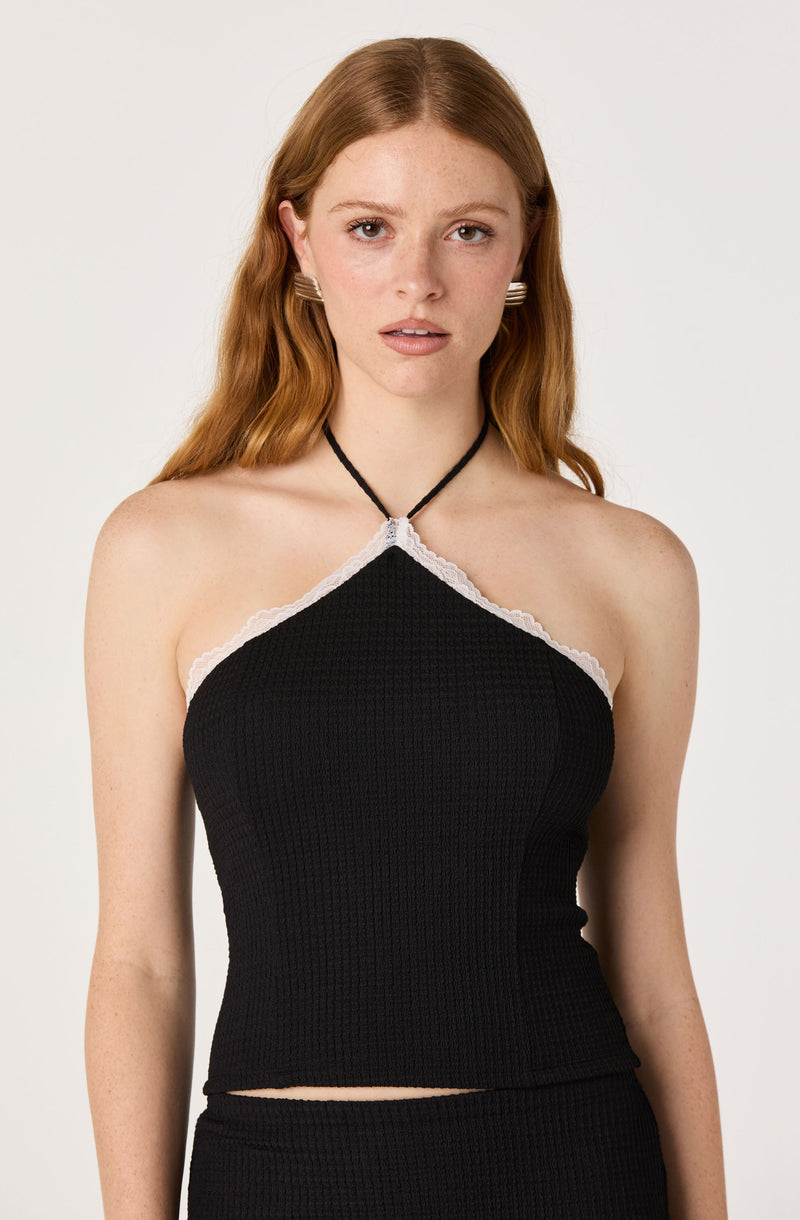 Woman wearing a black halter top with white lace trim around the neckline.