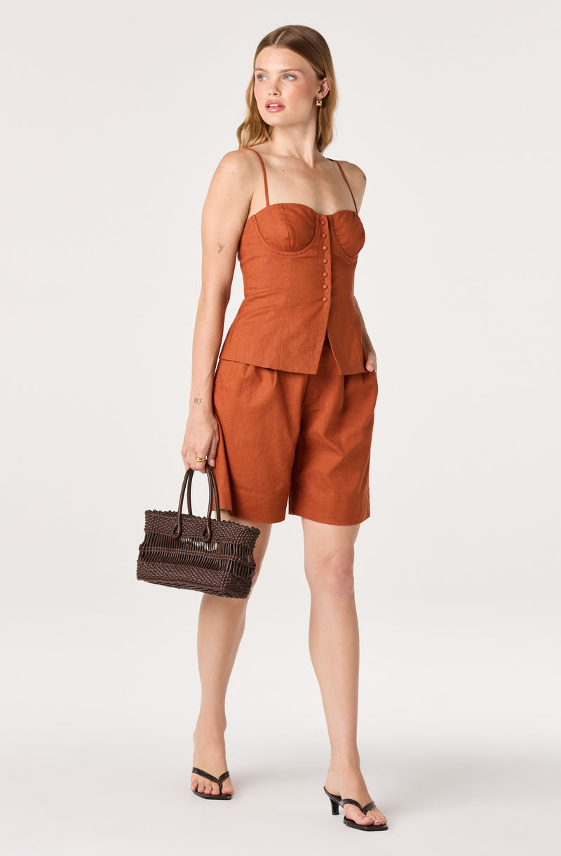 Woman wearing a rust-colored halter top and matching shorts, carrying a woven handbag.