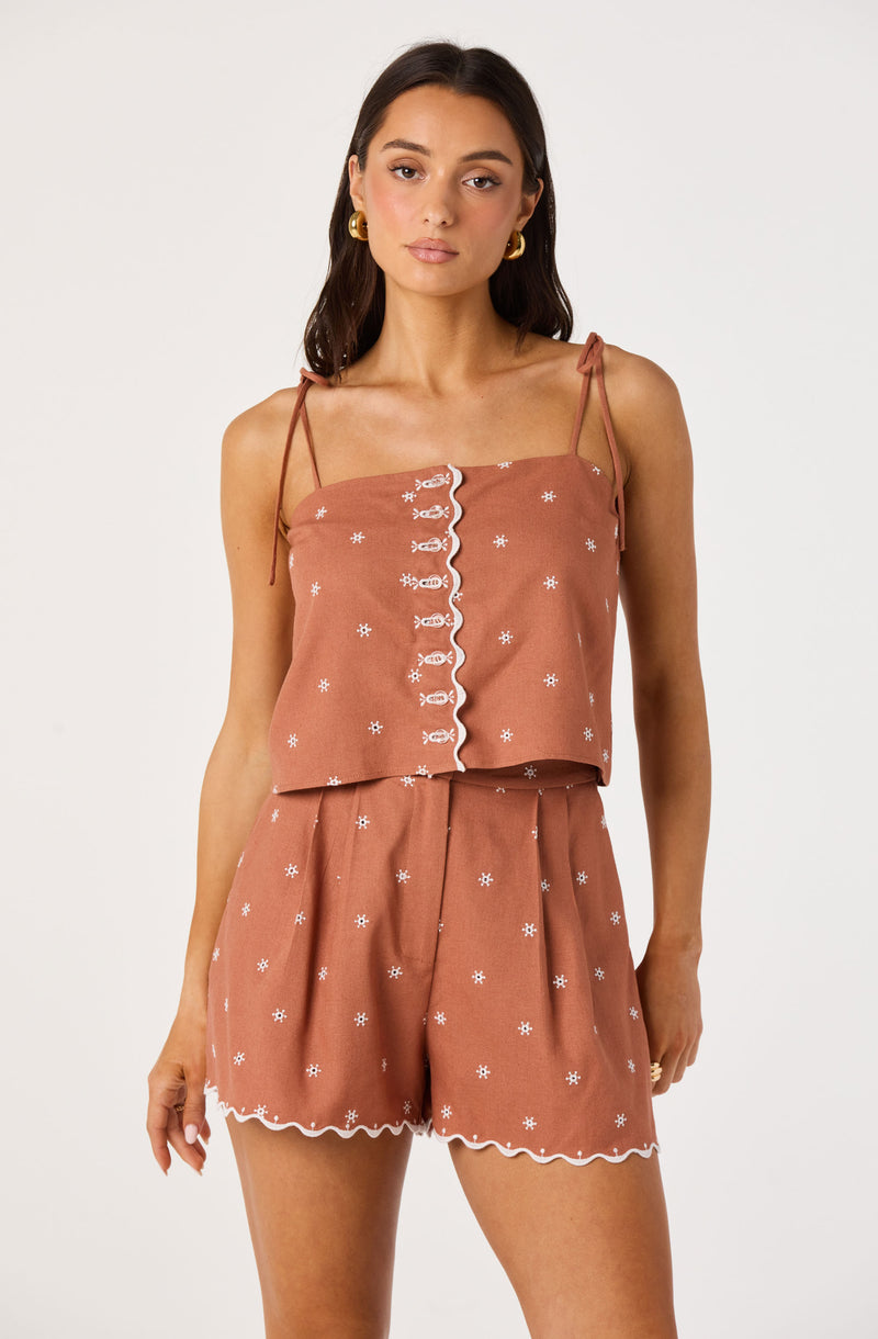 Woman in a rust-colored, two-piece summer outfit with white embroidery, spaghetti straps on top.